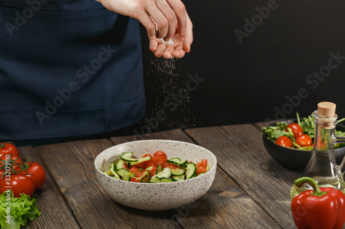 Woman salting fresh healthy vegetable salad on wooden table. Female hands with copyspace.