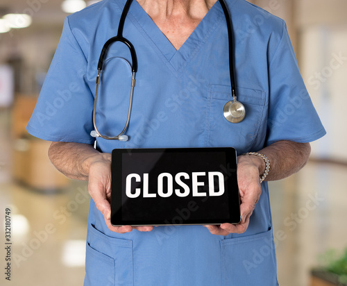 Senior male caucasian doctor with stethoscope in medical scrubs holding electronic tablet for saying hospital is closed due to coronavirus photo