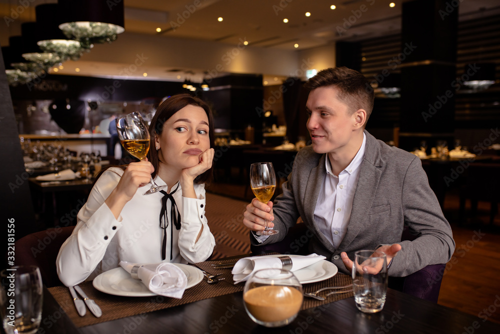 couple in restaurant. bored caucasian woman and man interested on rendezvous. gentleman try to entertain his girlfriend, she sit thinking about something about with glass of champagne