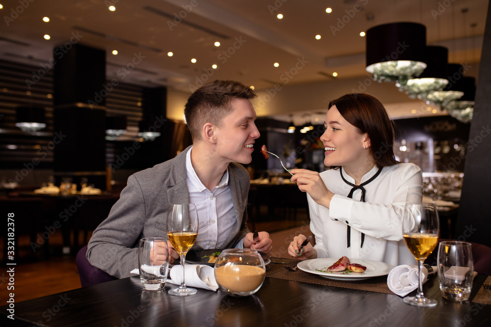 young caucasian married couple treating food with each other in restaurant. happy man and woman try delicious tasty food, dessert cooked by professional cook