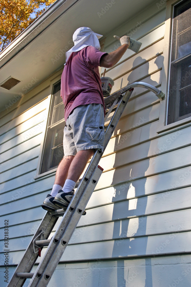 Man Balances On Ladder While Painting a House Exterior