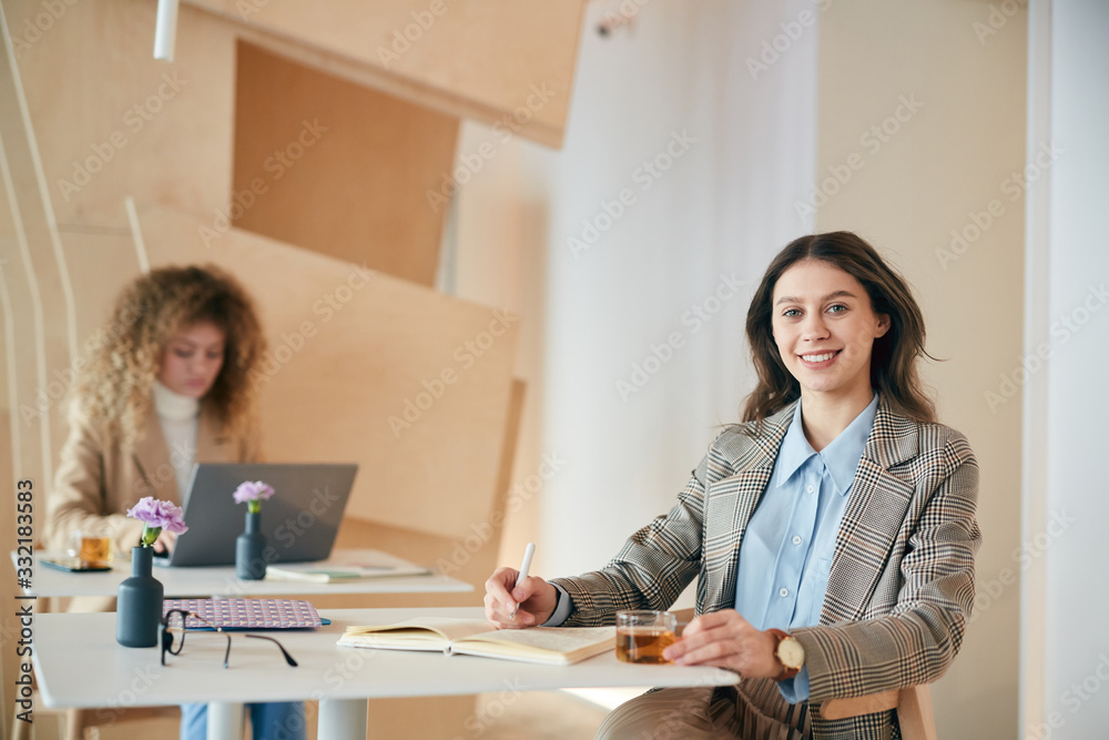 Portrait of smiling female student smiling at camera while studying in college cafe, copy space Portrait of smiling female student smiling at camera while studying in college cafe, copy space