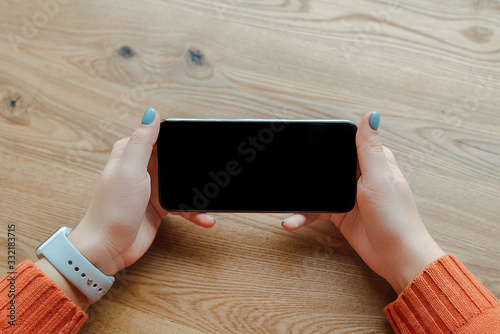cropped view of girl using smartphone with blank screen on wooden table
