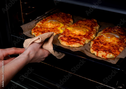 Khachapuri. A traditional Georgian dish with cheese, cottage cheese and eggs. Bakery products. A woman takes a dish out of the oven.
