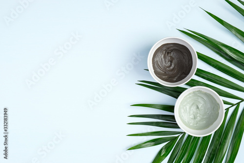 SPA facial mask products and green tropical leaf on paste blue background. Cosmetic mud mask in glass bowls, clay face mask. Face skin care and beauty treatment concept