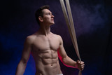 Muscular male circus artist with aerial straps on black and smoked background