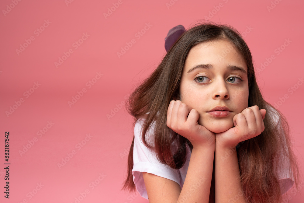 Sad brunette girl lies on the ground leaned on her hands and looking at left side, isolated over pink background Sad brunette girl lies on the ground leaned on her hands and looking at left side, isolated over pink background