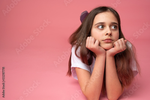 Surprised brunette female lies on the ground leaned on her hands and looking at the right side, isolated over pink background