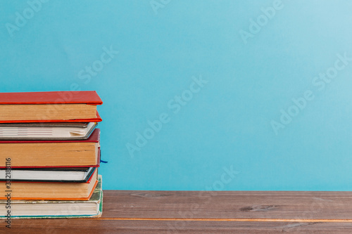 A simple composition of many hardback books  raw books on a wooden table and a bright blue background. Going back to school. Copy space. Education.
