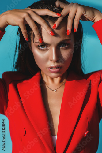 Fototapeta Portrait of a beautiful woman in a red jacket with red nails on a blue backgroun