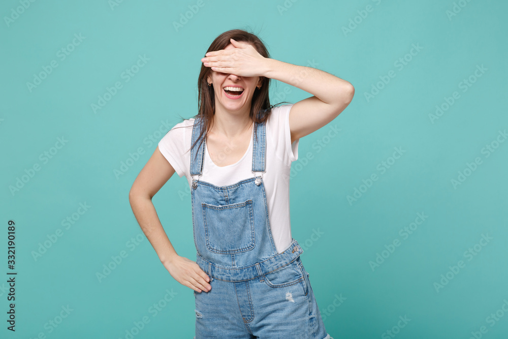 Cheerful young brunette woman girl in casual denim clothes posing isolated on blue turquoise wall background studio portrait. People lifestyle concept. Mock up copy space. Covering eyes with hand. Cheerful young brunette woman girl in casual denim clothes posing isolated on blue turquoise wall background studio portrait. People lifestyle concept. Mock up copy space. Covering eyes with hand.