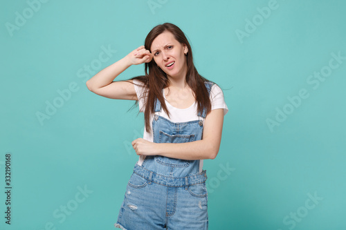 Dissatisfied young brunette woman girl in casual denim clothes posing isolated on blue turquoise wall background studio portrait. People lifestyle concept. Mock up copy space. Crying, wiping tears.