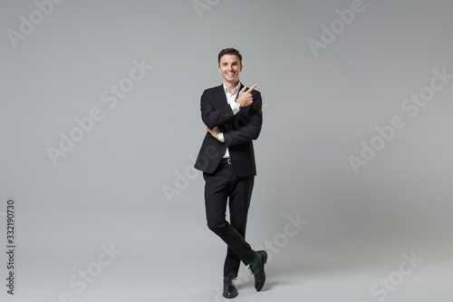 Smiling young business man in classic black suit shirt posing isolated on grey background studio portrait. Achievement career wealth business concept. Mock up copy space. Pointing index finger up.
