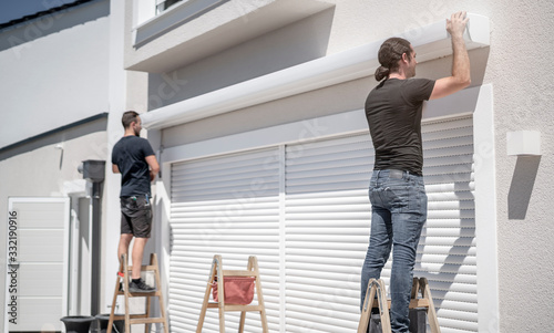 Fotografi zwei Handwerker hängen eine Markise an den Halterungen an der Hauswand ein
