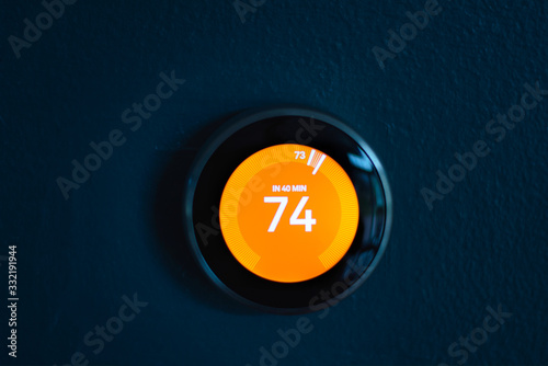 Nest smart home thermostat with red center in heat mode. Saving energy heating home. Isolated product on blue wall
