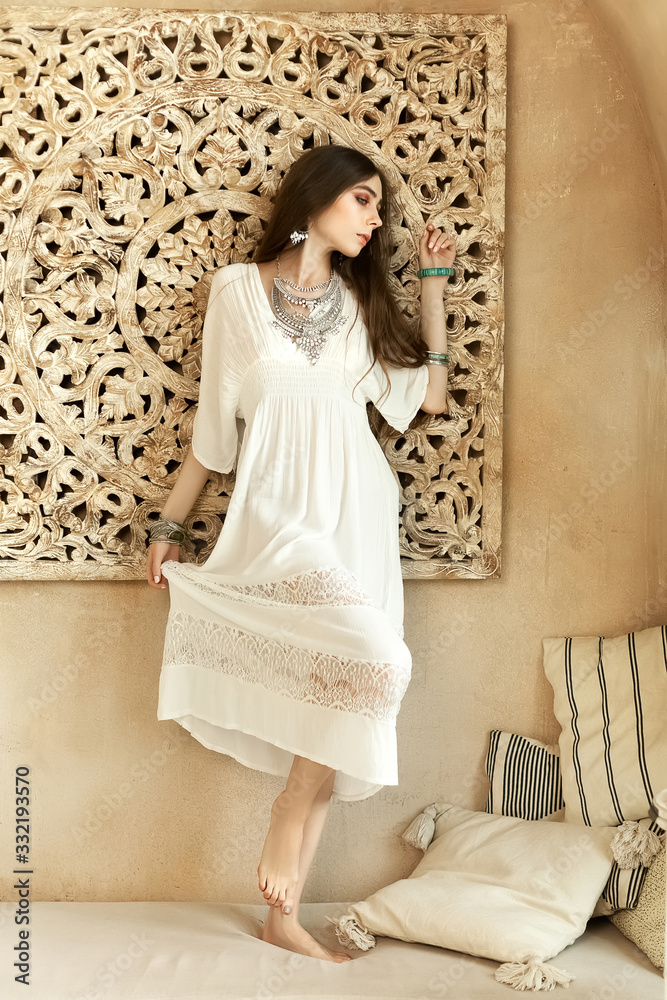 Fototapeta premium Beautiful girl in white dress and stylish jewelry inside room middle eastern interior