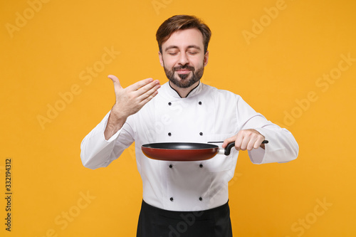 Fotótapéta Smiling young bearded male chef cook or baker man in white uniform isolated on yellow background