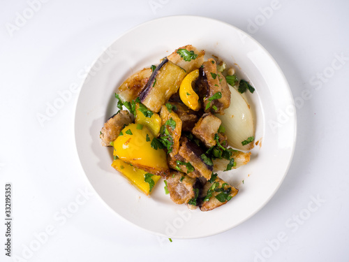 Hot eggplant and yellow pepper salad on a round white plate. Top view