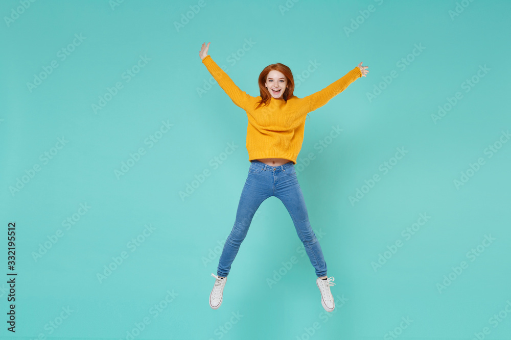 Funny young redhead woman girl in yellow knitted sweater posing isolated on blue turquoise background studio portrait. People lifestyle concept. Mock up copy space. Jumping spreading hands and legs. Funny young redhead woman girl in yellow knitted sweater posing isolated on blue turquoise background studio portrait. People lifestyle concept. Mock up copy space. Jumping spreading hands and legs.