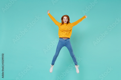 Funny young redhead woman girl in yellow knitted sweater posing isolated on blue turquoise background studio portrait. People lifestyle concept. Mock up copy space. Jumping spreading hands and legs.