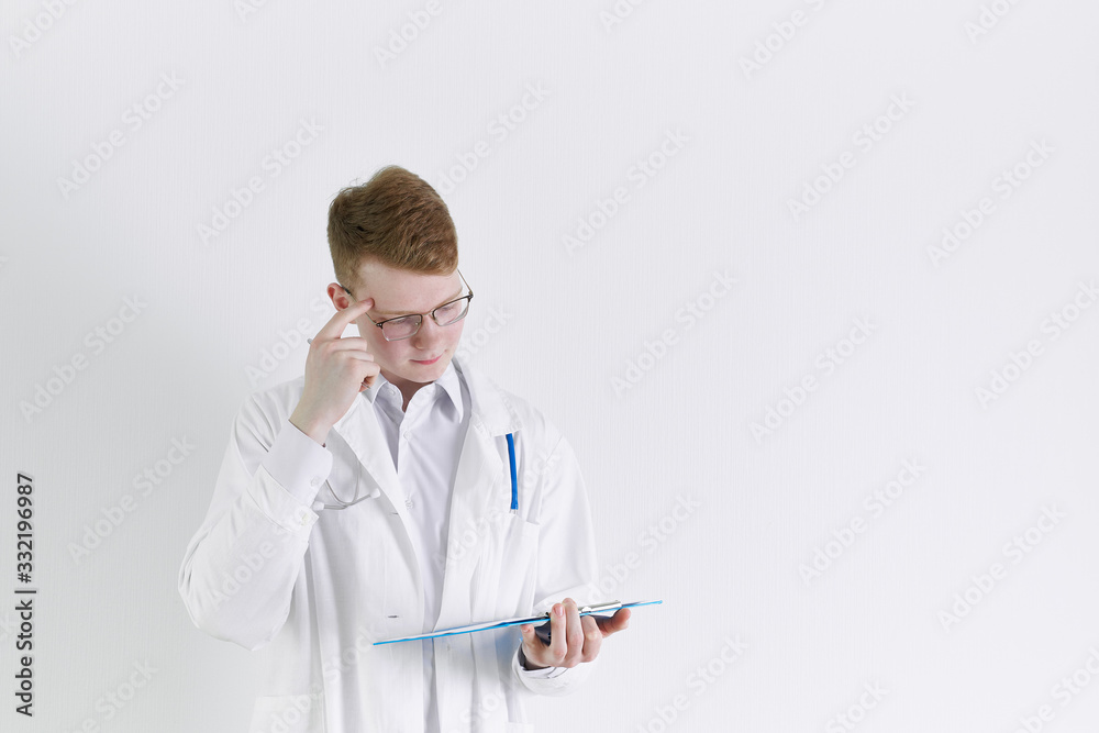 Young trainee doctor intern stands on white background. Handsome red- haired man, thinking Young trainee doctor intern stands on white background. Handsome red- haired man, thinking