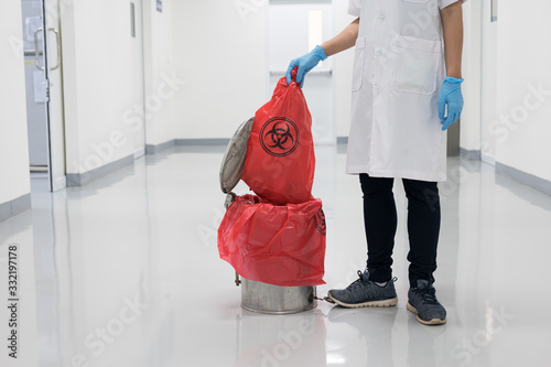 Scientist wearing blue gloves and red bag with bioharzard sign.A woman worker hand holding red garbage bag.Maid and infection waste bin at the indoor public building.Infectious control.