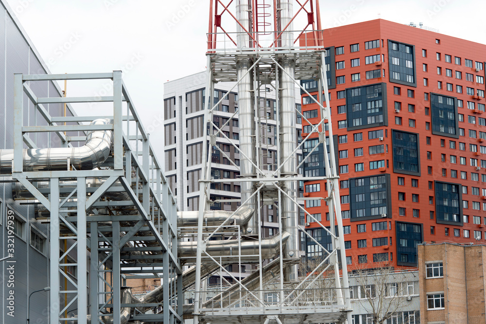 The exterior of the boiler room with the output of shiny metal pipes against the background of a number of buildings. The exterior of the boiler room with the output of shiny metal pipes against the background of a number of buildings.