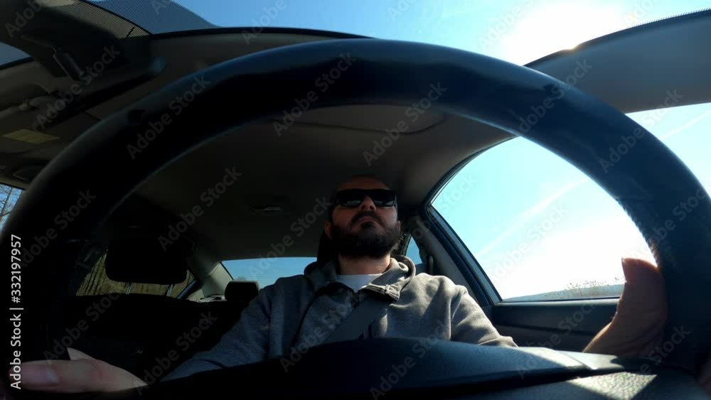 Man in hoodie with sunglasses driving a car, wide angle view through the steering wheel Man in hoodie with sunglasses driving a car, wide angle view through the steering wheel