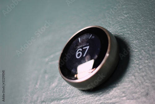 Nest smart home thermostat on blue wall from below. Green technology saves money heating and cooling in home