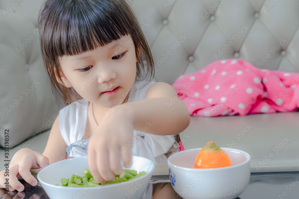 Child little girl eats vegetable salad using hand. Portrait of cheerful asian girl eating salad with joy. She is looking aside with curiosity and smiling. Child little girl eats vegetable salad using hand. Portrait of cheerful asian girl eating salad with joy. She is looking aside with curiosity and smiling.