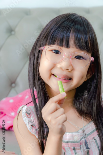 Portrait of cheerful asian girl eating salad with joy. She is looking aside with curiosity and smiling. Eating vegetables by child make them healthier