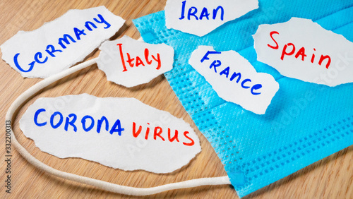 Medical face mask with coronavirus inscription on paper on yellow table. Italy, France, Spain, Germany and Iran. Novel coronavirus pneumonia 2019-nCoV or COVID-19. Wuhan's seafood market virus