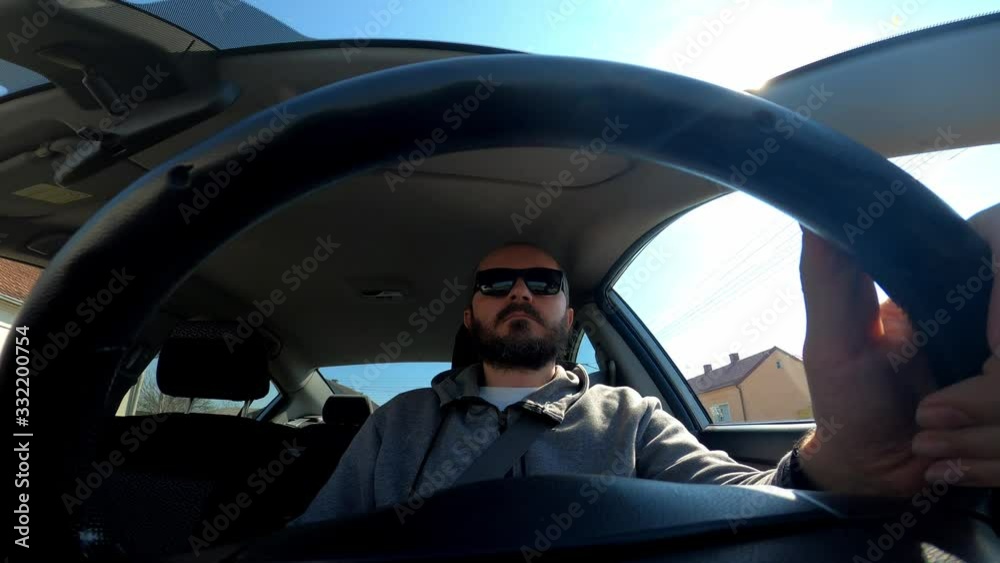 Man in hoodie and with sunglasses driving a car, wide angle view through the steering wheel
