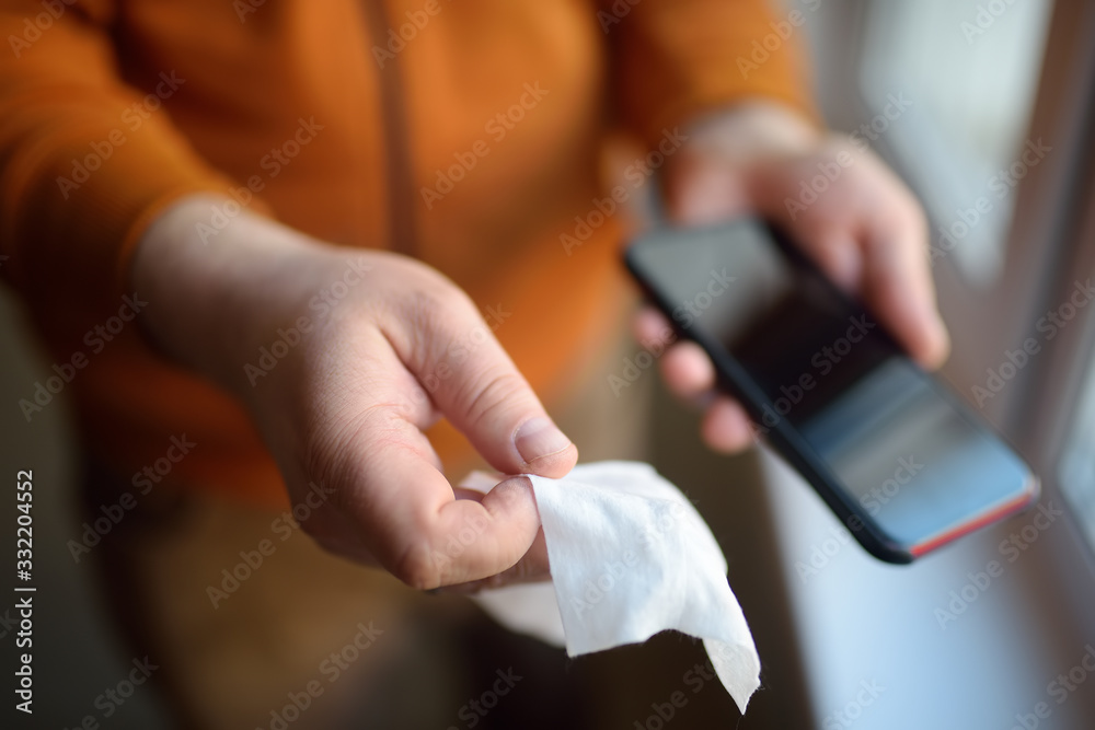 Obraz premium Mature man wipes with a disinfecting cloth heis smartphone after returning home. Safety during COVID-19 outbreak in public places. Epidemic of virus covid.