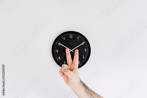 clock on white wall with one hand making peace gesture front of clock