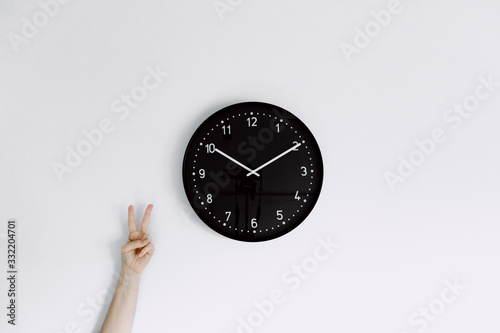  clock on white wall with one hand making peace gesture next to clock