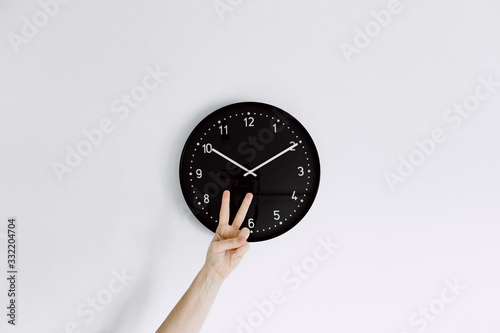  clock on white wall with one hand making peace gesture front of clock