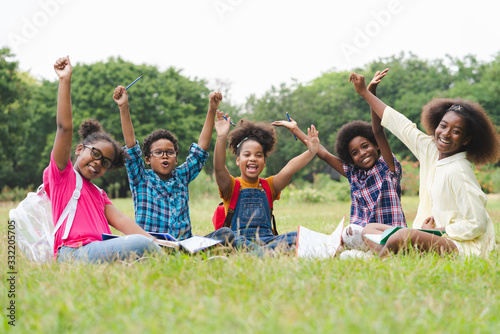 Happy fun group of African American children raised hands while practice drawing in a book and sitting in the park. Education outdoor concept.