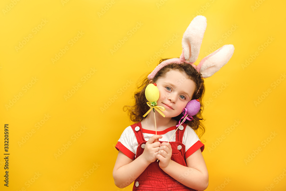 Cheerful little girl with bunny fluffy ears, prepares for unforgettable spring holiday, dressed in white t-shirt, models over yellow background. People, special holiday, celebration, Easter concept Cheerful little girl with bunny fluffy ears, prepares for unforgettable spring holiday, dressed in white t-shirt, models over yellow background. People, special holiday, celebration, Easter concept