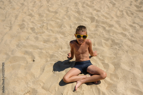 Little boy in sunglasses on the beach. Child in swimming trunks on the sea sand.