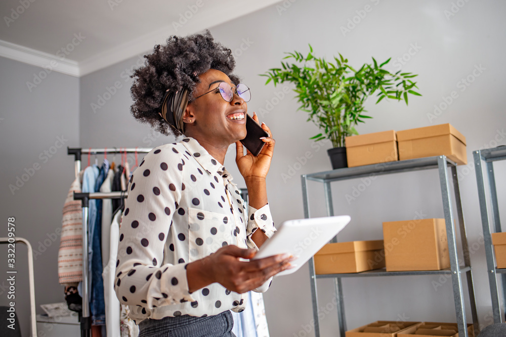Beautiful afro american young woman using a digital tablet in an office, receiving good news, smiling. Portrait of a smiling young woman working at home with laptop and mobile phone Beautiful afro american young woman using a digital tablet in an office, receiving good news, smiling. Portrait of a smiling young woman working at home with laptop and mobile phone