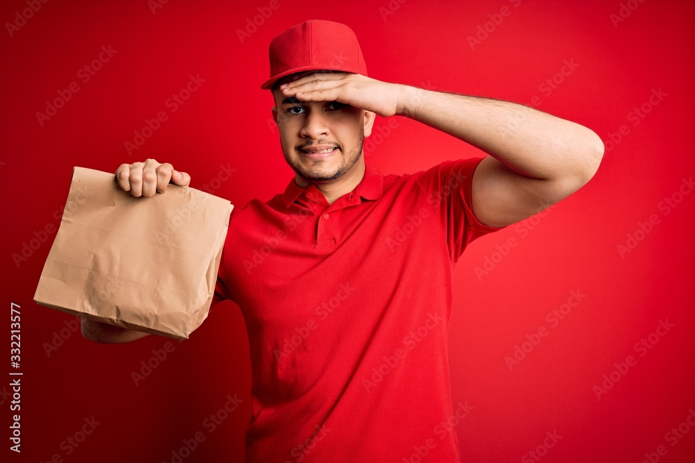 Young handsome delivery man holding paper bag with takeaway food over red background stressed with hand on head, shocked with shame and surprise face, angry and frustrated. Fear and upset for mistake. Young handsome delivery man holding paper bag with takeaway food over red background stressed with hand on head, shocked with shame and surprise face, angry and frustrated. Fear and upset for mistake.