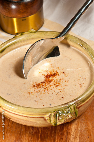 Top view, close up of a artisan, ceramic bowl of turkey, cauliflower and apple soup with an artisan spoon scooping the soup with peppereca, on top and a wood salt griner in background photo