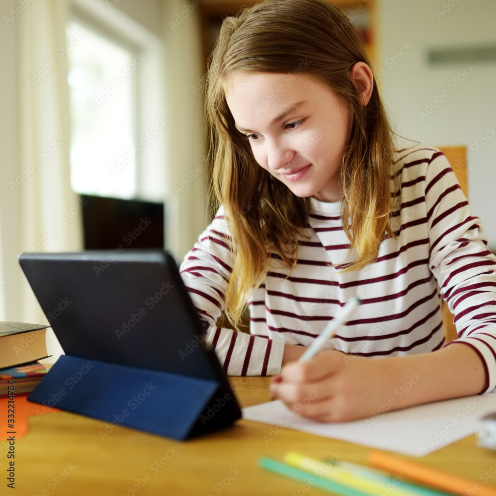 Smart preteen schoolgirl doing her homework with digital tablet at home. Education and distance learning for kids. Homeschooling during quarantine. Smart preteen schoolgirl doing her homework with digital tablet at home. Education and distance learning for kids. Homeschooling during quarantine.