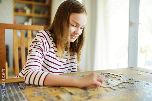 Cute young girl playing puzzles at home. Child connecting jigsaw puzzle pieces in a living room table. Kid assembling a jigsaw puzzle. Fun family leisure.