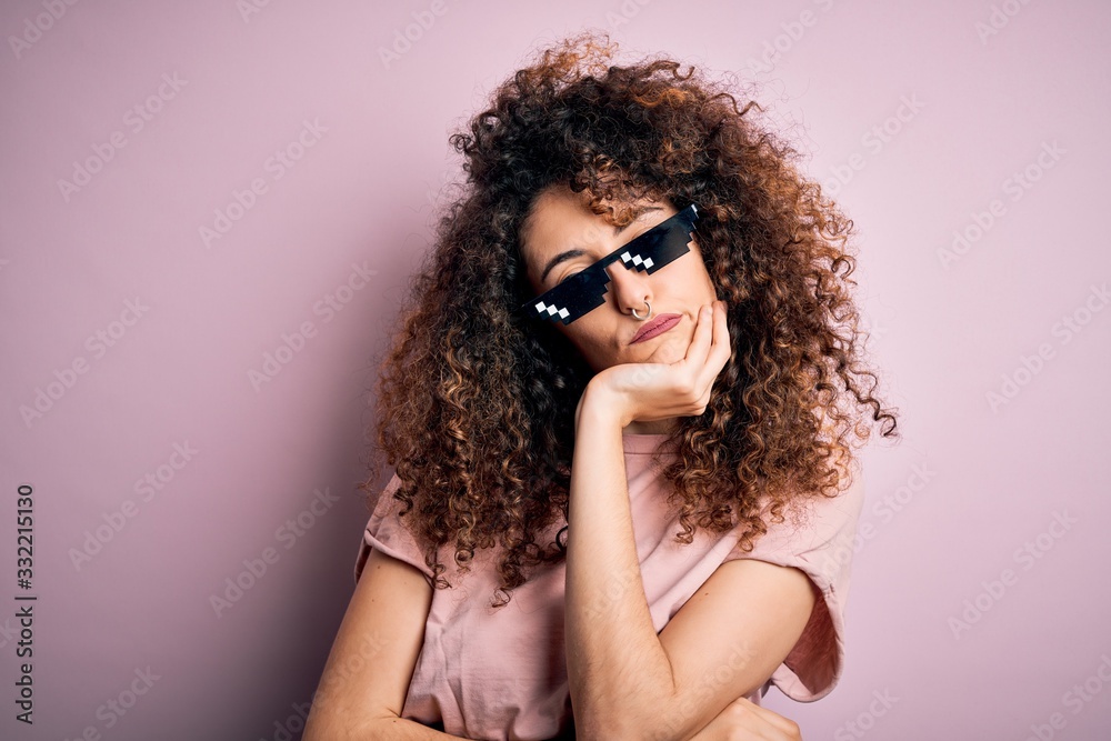 Young beautiful woman with curly hair and piercing wearing funny thug life sunglasses thinking looking tired and bored with depression problems with crossed arms. Young beautiful woman with curly hair and piercing wearing funny thug life sunglasses thinking looking tired and bored with depression problems with crossed arms.