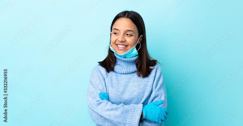 Young brunette mixed race woman protecting from the coronavirus with a mask and gloves over isolated blue background looking to the side Young brunette mixed race woman protecting from the coronavirus with a mask and gloves over isolated blue background looking to the side
