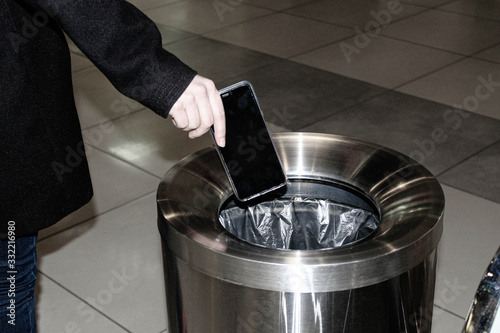 A girl passing by a garbage can throws out a smartphone.