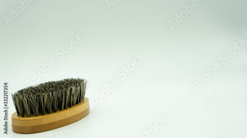 Close-up of bamboo beard brush with natural bristles on white background on the left of the image with space on the right for text. Facial care concept for men