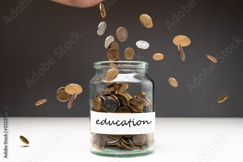 Coins in a jar with education text on a white label. Money falling from the sky above. Savings abstract concept. Copy space.